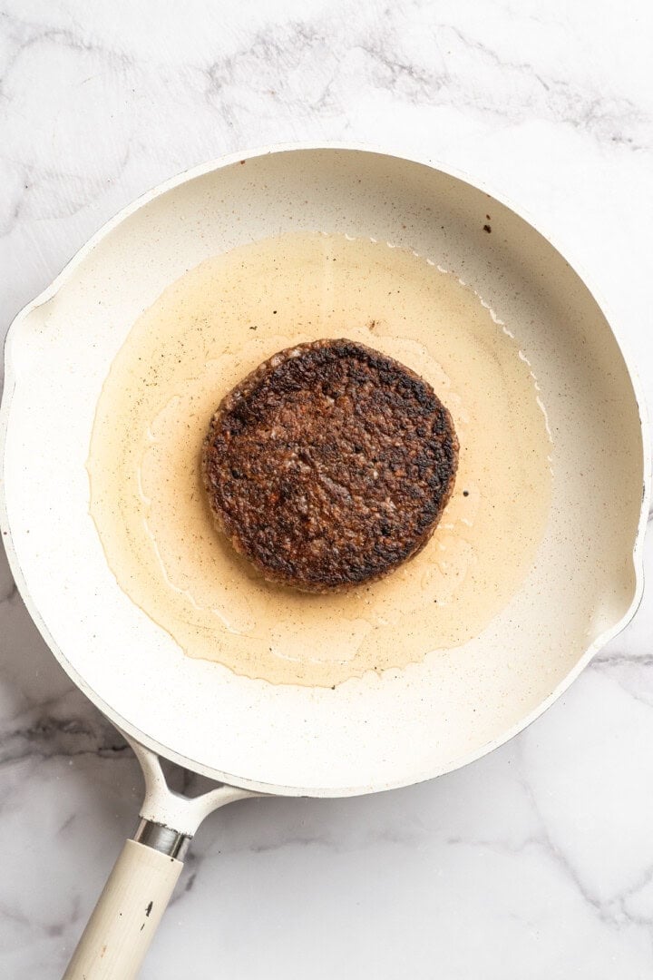Beet burger patty cooking in skillet of oil.