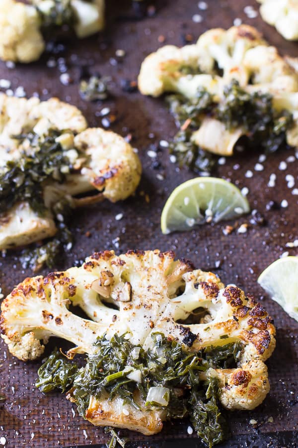 Cauliflower steaks on a baking sheet, with a lemon wedge. 