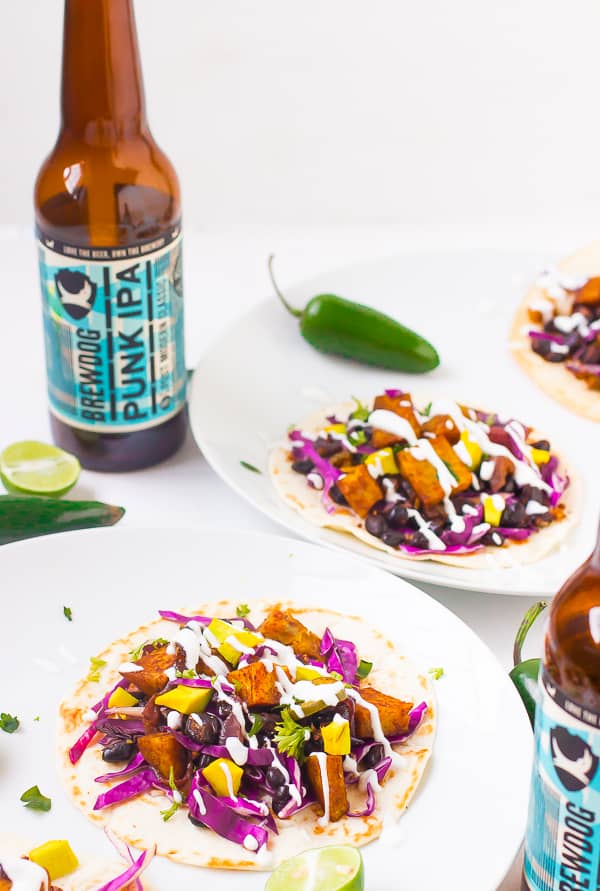 Sweet potato and black bean tacos on white plates with bottles of beers. 