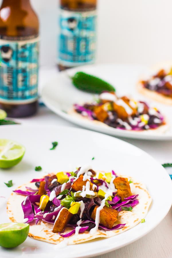 Black bean and sweet potato tacos on a white plate with wedges of lime. 