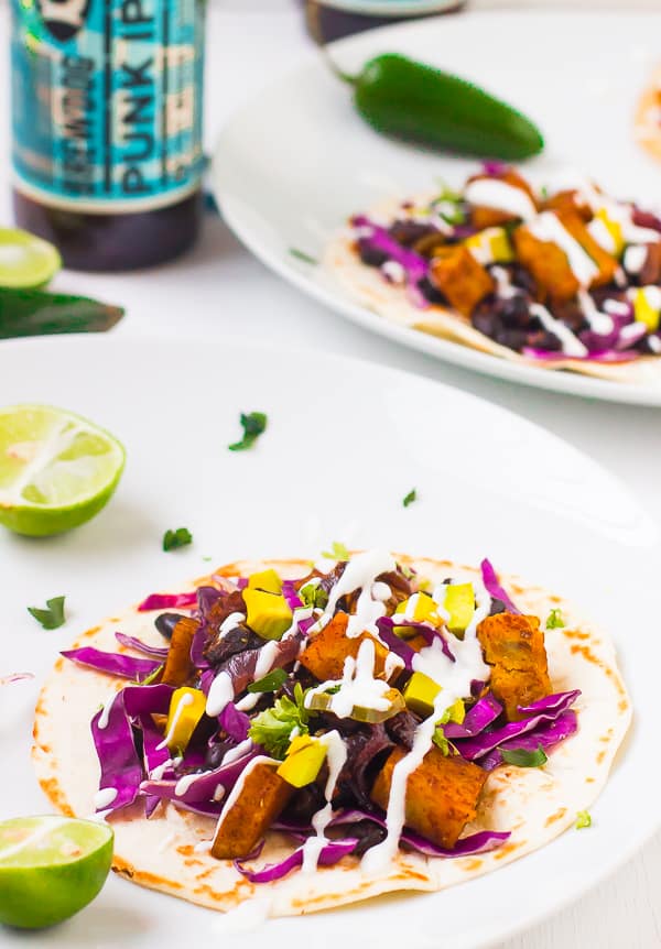 Black bean and sweet potato taco on a white plate with a wedge of lime. 