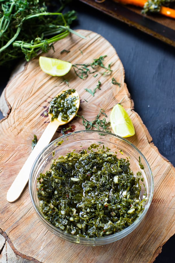 A bowl of carrot greens chimichurri with a spoon beside it. 