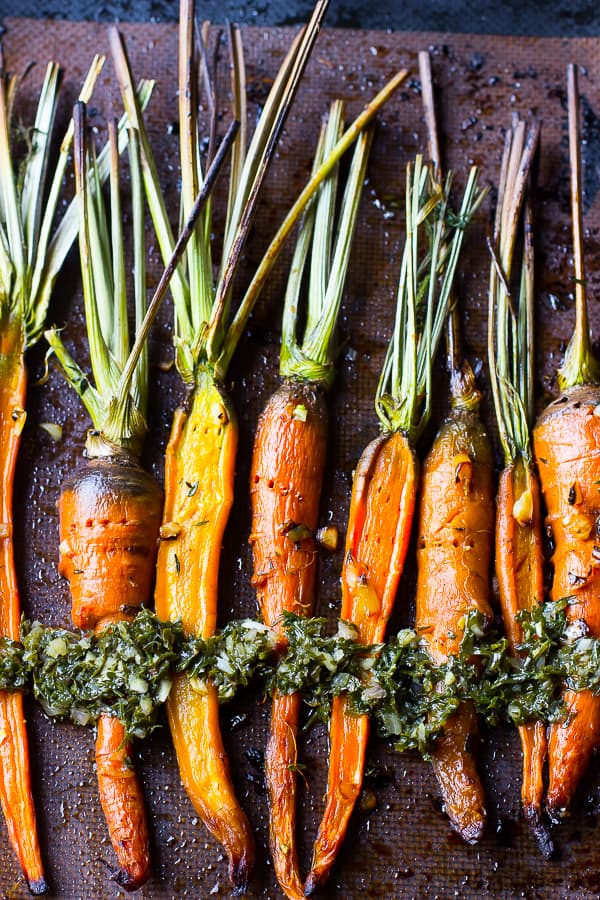 Overhead shot of of maple roasted carrots drizzled with chimichurri sauce on a baking sheet. 