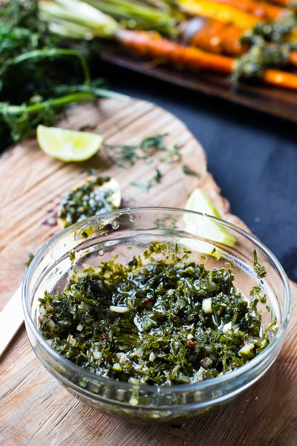 Chimichurri in a glass bowl on a wood board. 