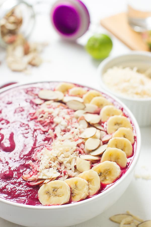 Banana berry beet smoothie bowl with sliced almonds and sliced bananas on top.