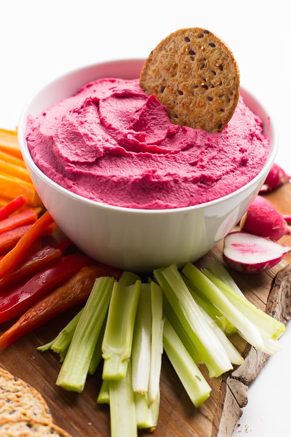 A cracker dipped into a white bowl of beet hummus. 
