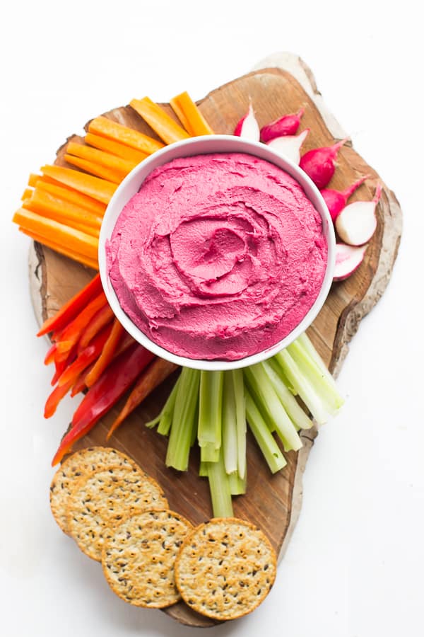 Overhead shot of beet hummus, with vegetables and crackers around it. 