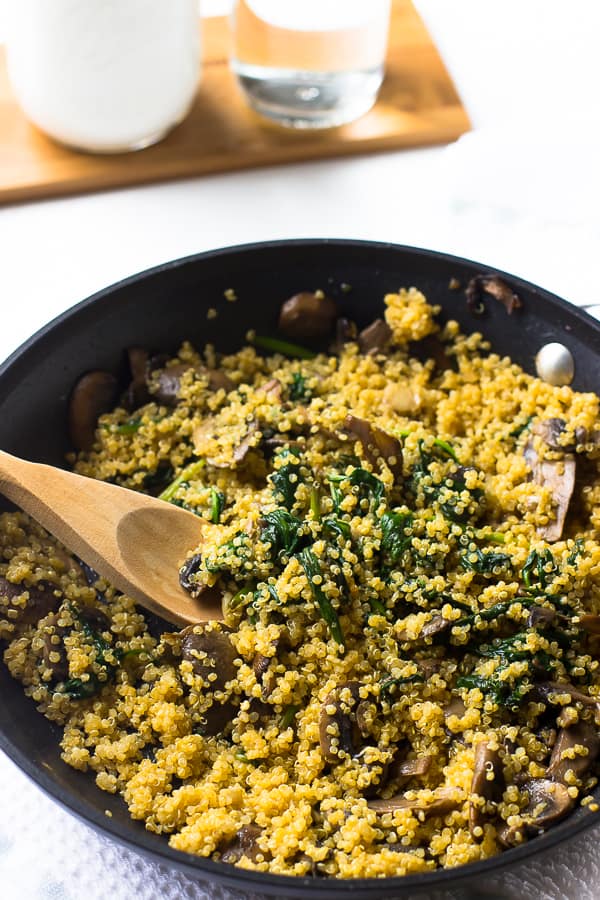 Spoon stirring creamy coconut spinach and mushroom quinoa in a black skillet. 