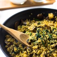 Creamy coconut spinach and mushroom quinoa with a wooden spoon in a black skillet.