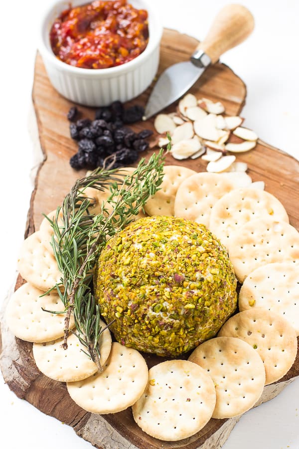 Top down shot of pistachio crusted vegan cheese ball on a wooden board with crackers.