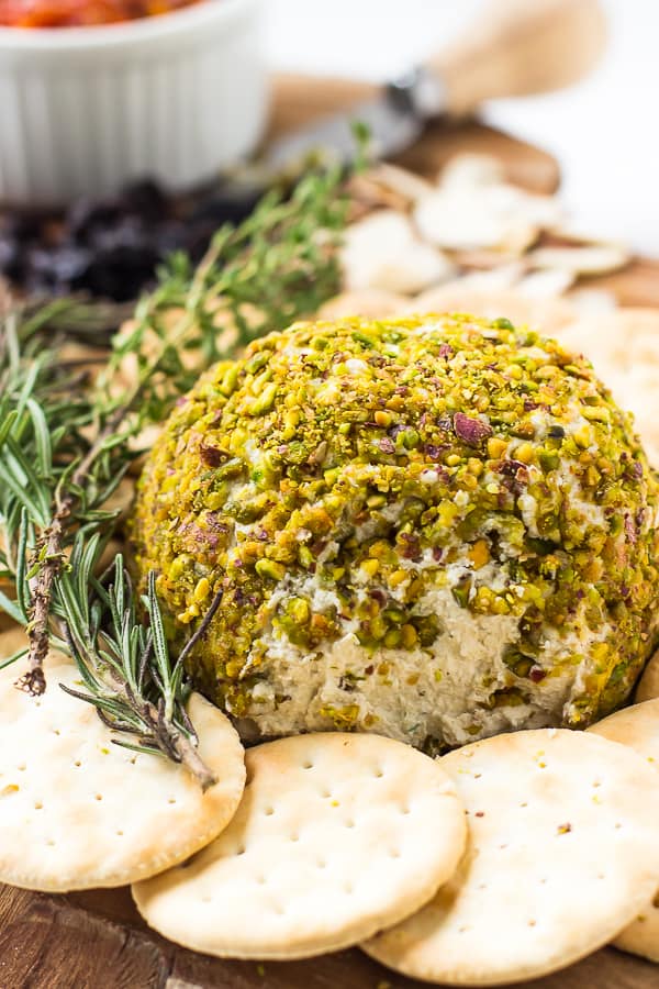 Pistachio crusted vegan cheese ball on a wood board with crackers. 