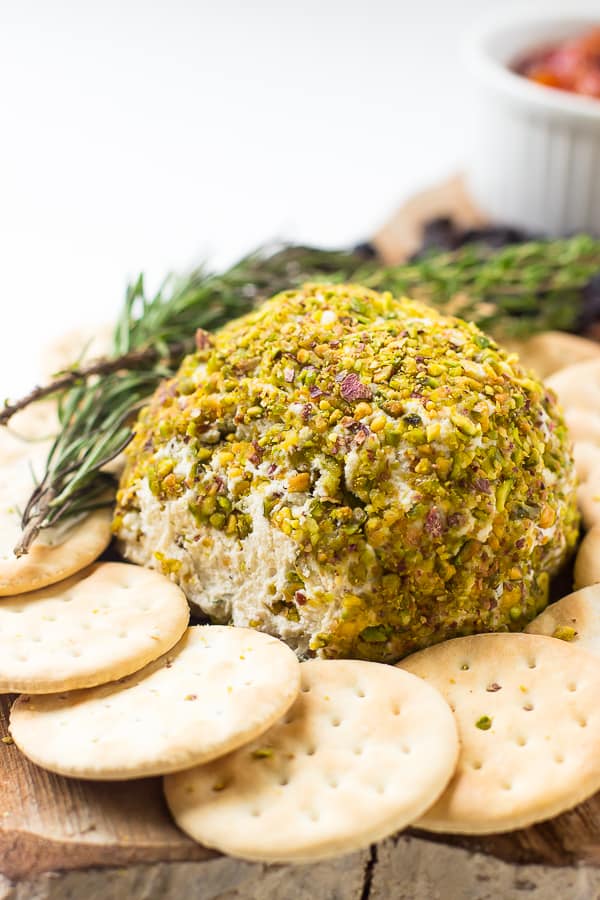 Pistachio crusted vegan cheese ball on a wooden board with crackers on the side.