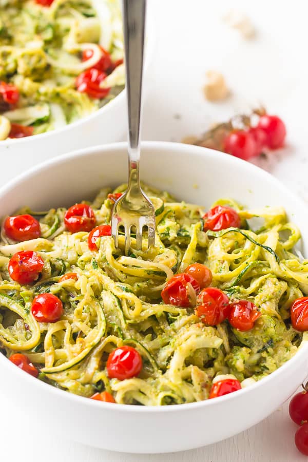 Pesto zucchini noodles in a white bowl with cherry tomatoes. 