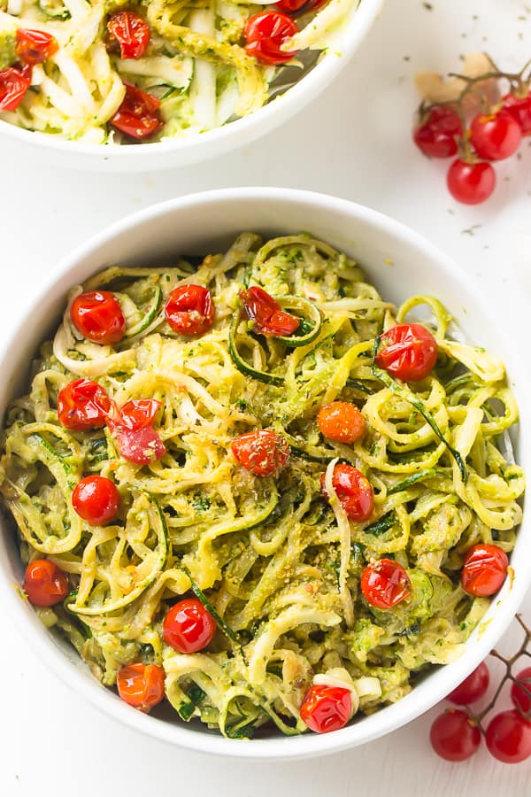 Overhead shot of pesto zucchini noodles with burst cherry tomatoes in a white bowl. 