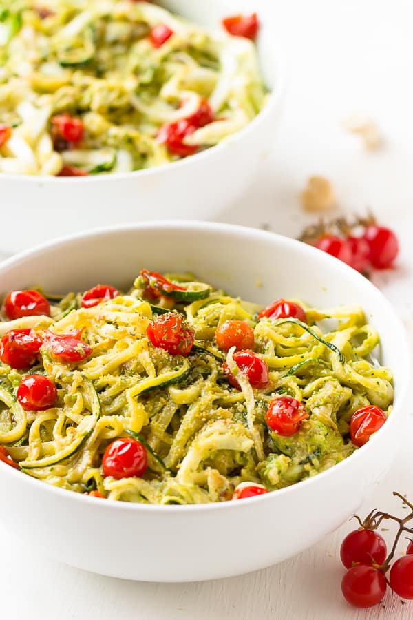 Two white bowls of pesto zucchini noodles on a white table.