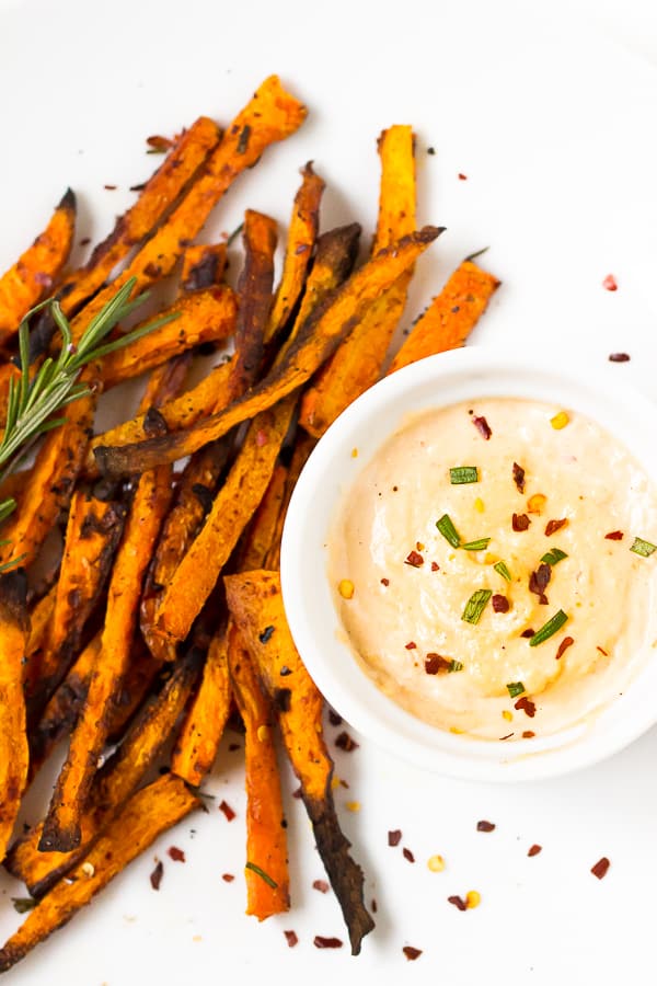 Top down shot of crispy baked carrot fries on white with harissa tahini dip in a ramekin.