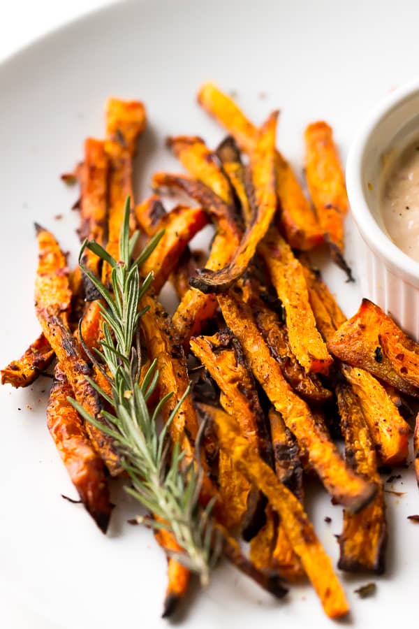 Carrot fries on a white plate with a sprig of rosemary.