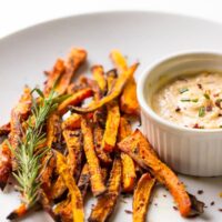 Baked carrot fries on a white plate with tahini dip on the side.