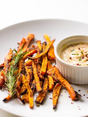 Baked carrot fries on a white plate with tahini dip on the side.
