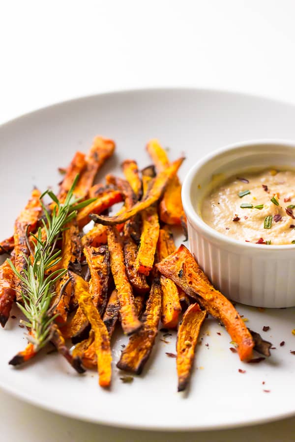 Crispy baked carrot fries on a white plate with harissa tahini dip in a white ramekin.