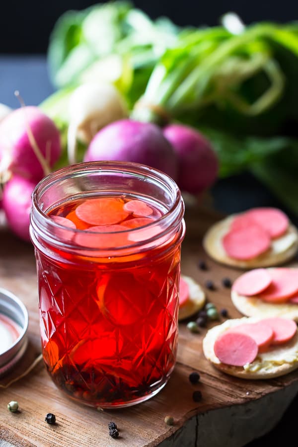  Quick pickled radishes in a glass on a wooden board.