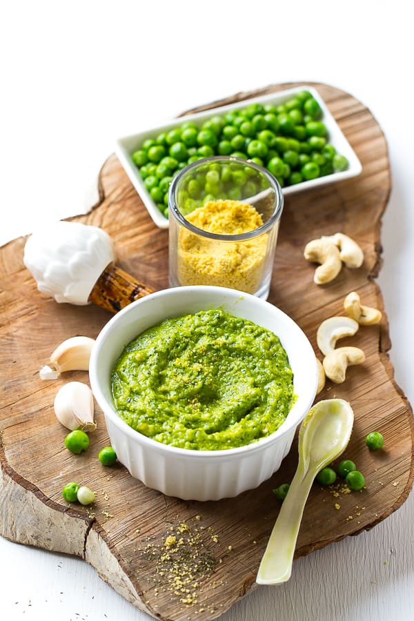 Cashew pea pesto in a white ramekin with ingredients around it. 