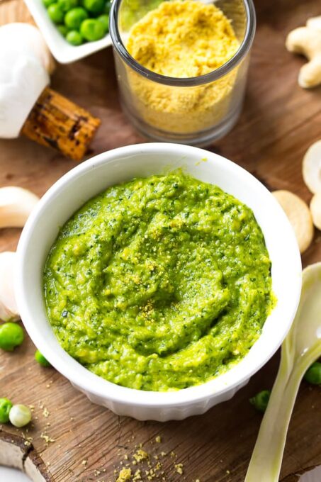 Top down shot of cashew pea pesto in a white ramekin on a wooden table. 