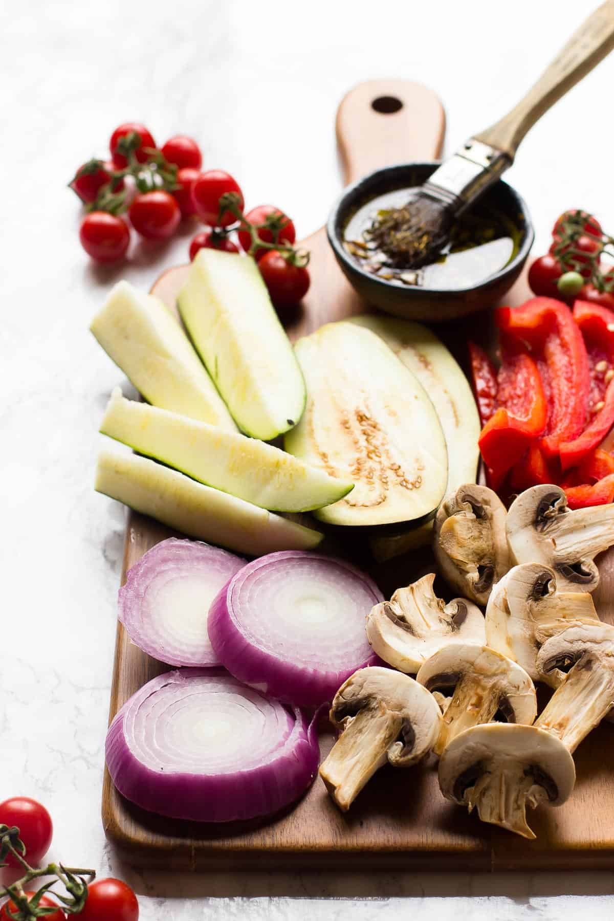 Side angle of raw veggies on a cutting board with brush and marinade.