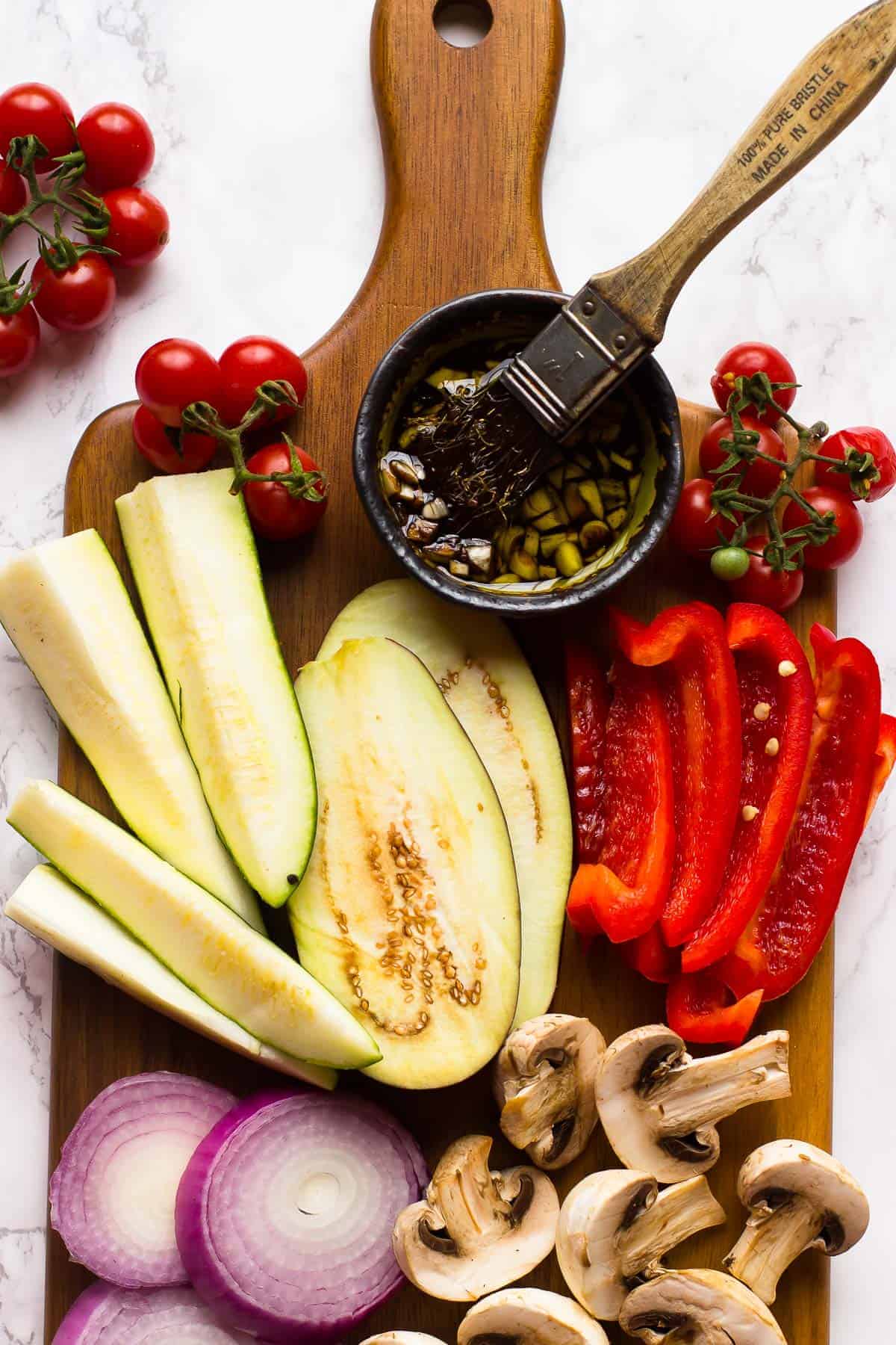 Raw vegetables on a cutting board with a brush in marinade.