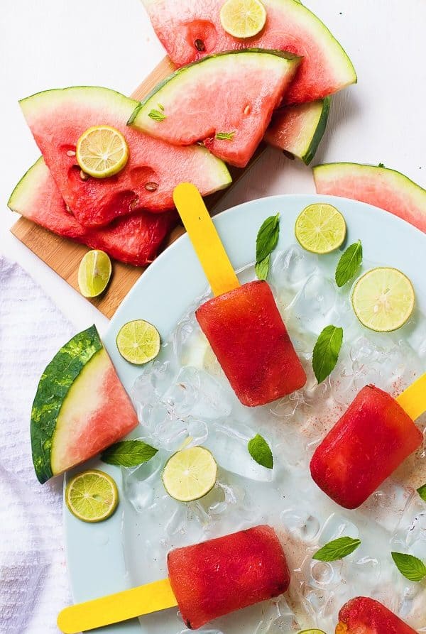 Top down shot of watermelon mint popsicles on a blue plate with slices of watermelon on the side. 