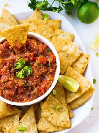Top down shot of salsa in a white ramekin with chips around it.