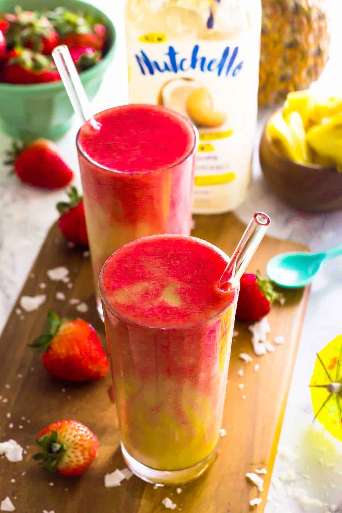 Two strawberry pineapple coconut smoothies on a wood board. 