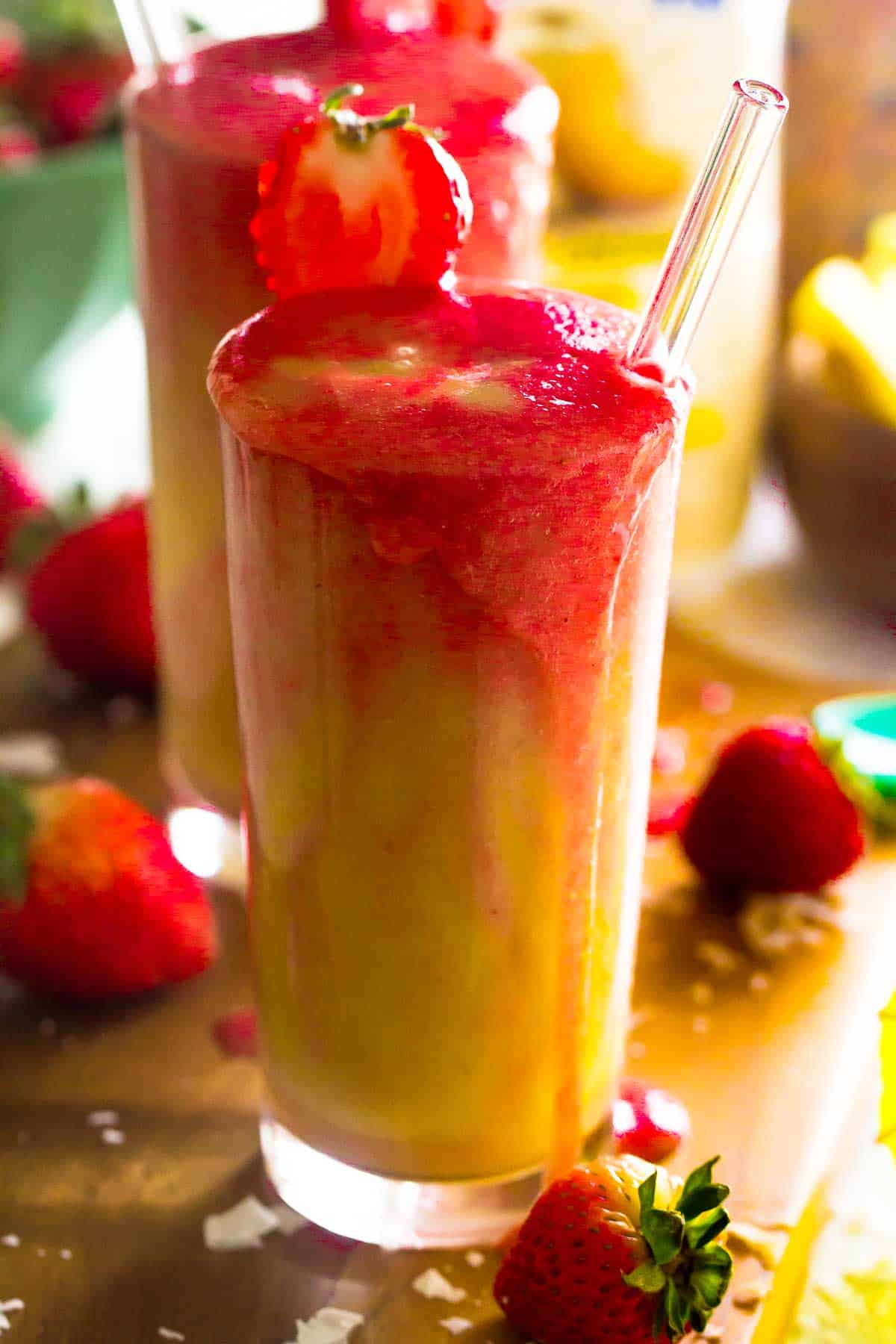 Side shot of two strawberry pineapple coconut smoothies on a wooden board.