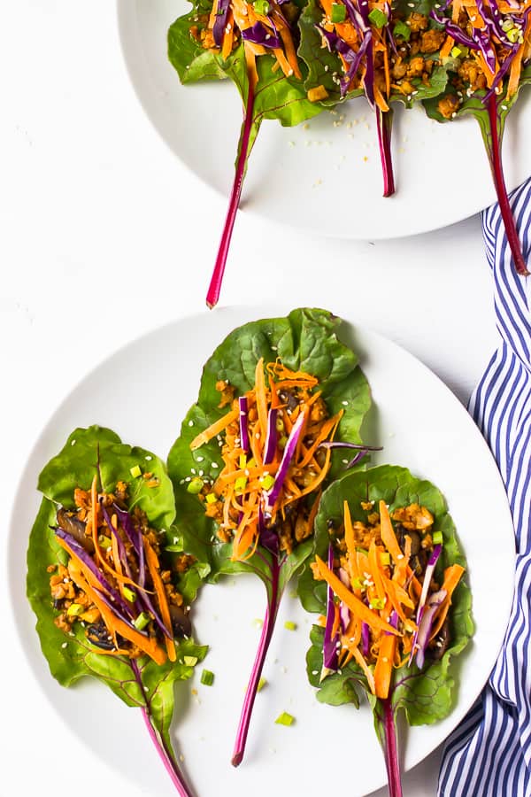 Overhead shot of three swiss chard wraps on a white plate with a striped cloth on the side. 