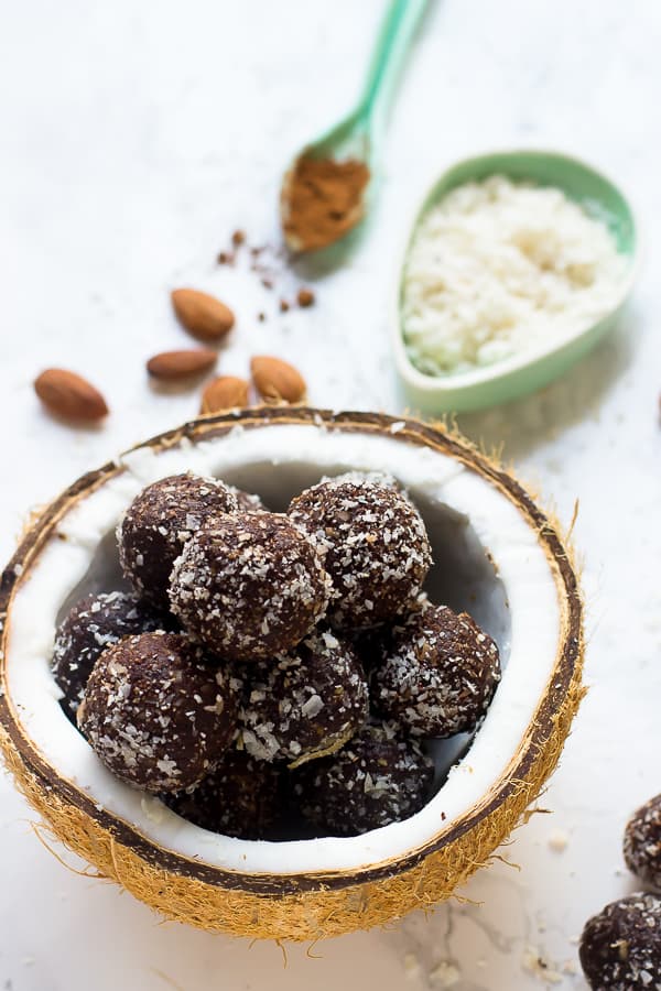 No bake brownie energy bites in a pile inside of a half of a dried coconut shell in front of ingredients.