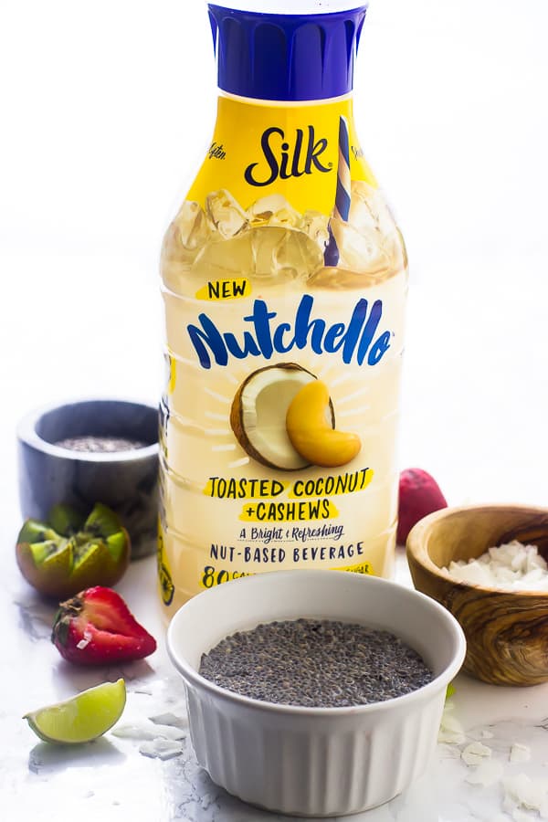 A bottle of nutchello nut milk on a table with chia seeds in ramekin. 