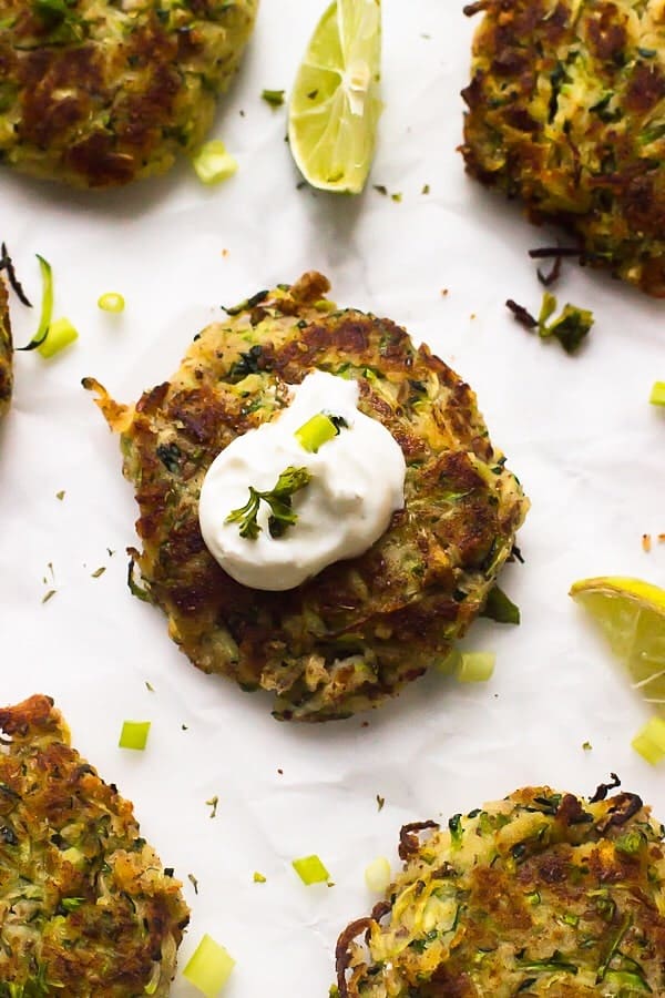 Overhead shot of zucchini fritters on a white table with lime wedges on the side.  