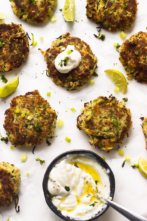 Overhead view of vegan zucchini fritters on parchment with bowl of dipping sauce