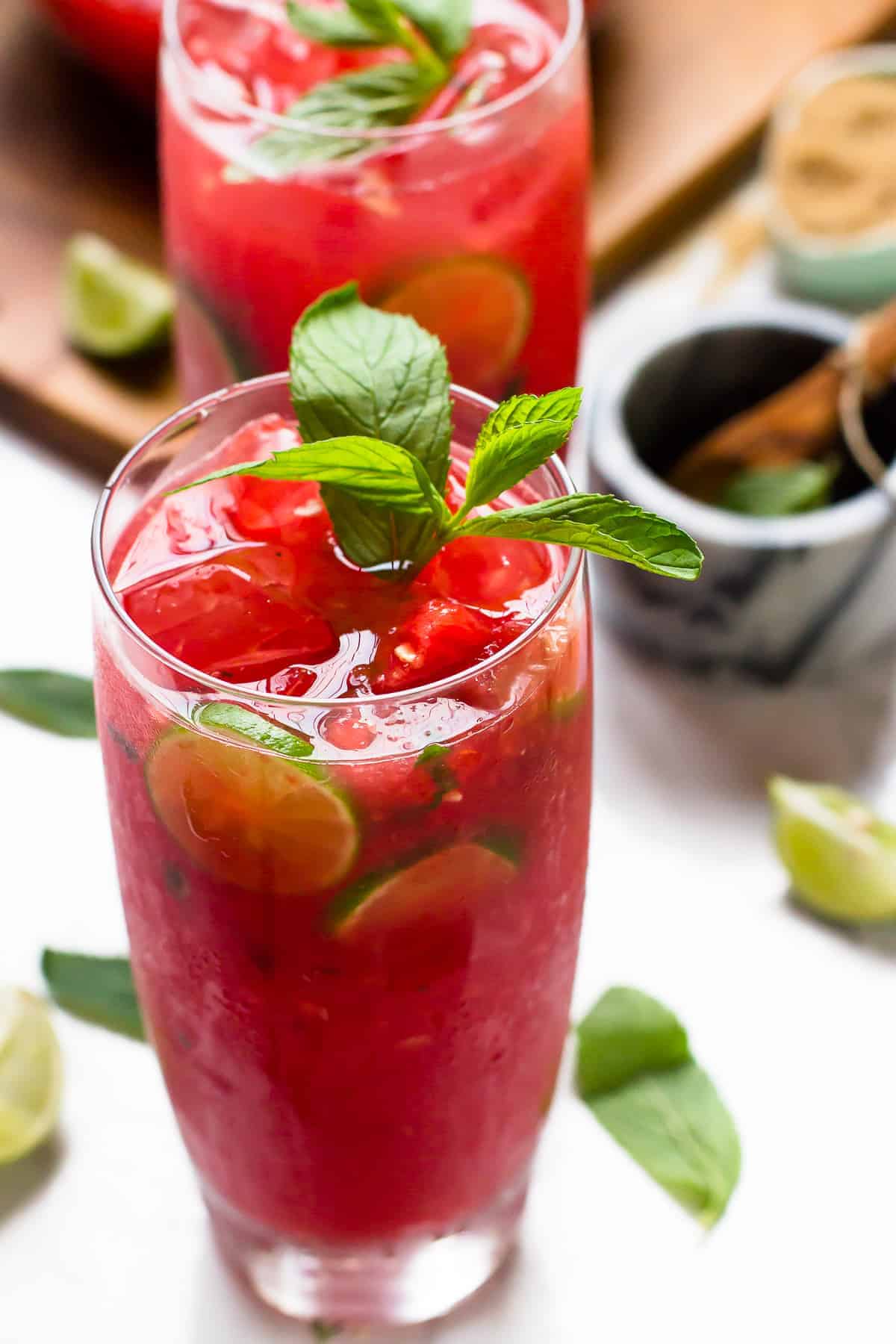 Side shot of watermelon mojitos in tall glasses with lime slices and sprigs of mint. 