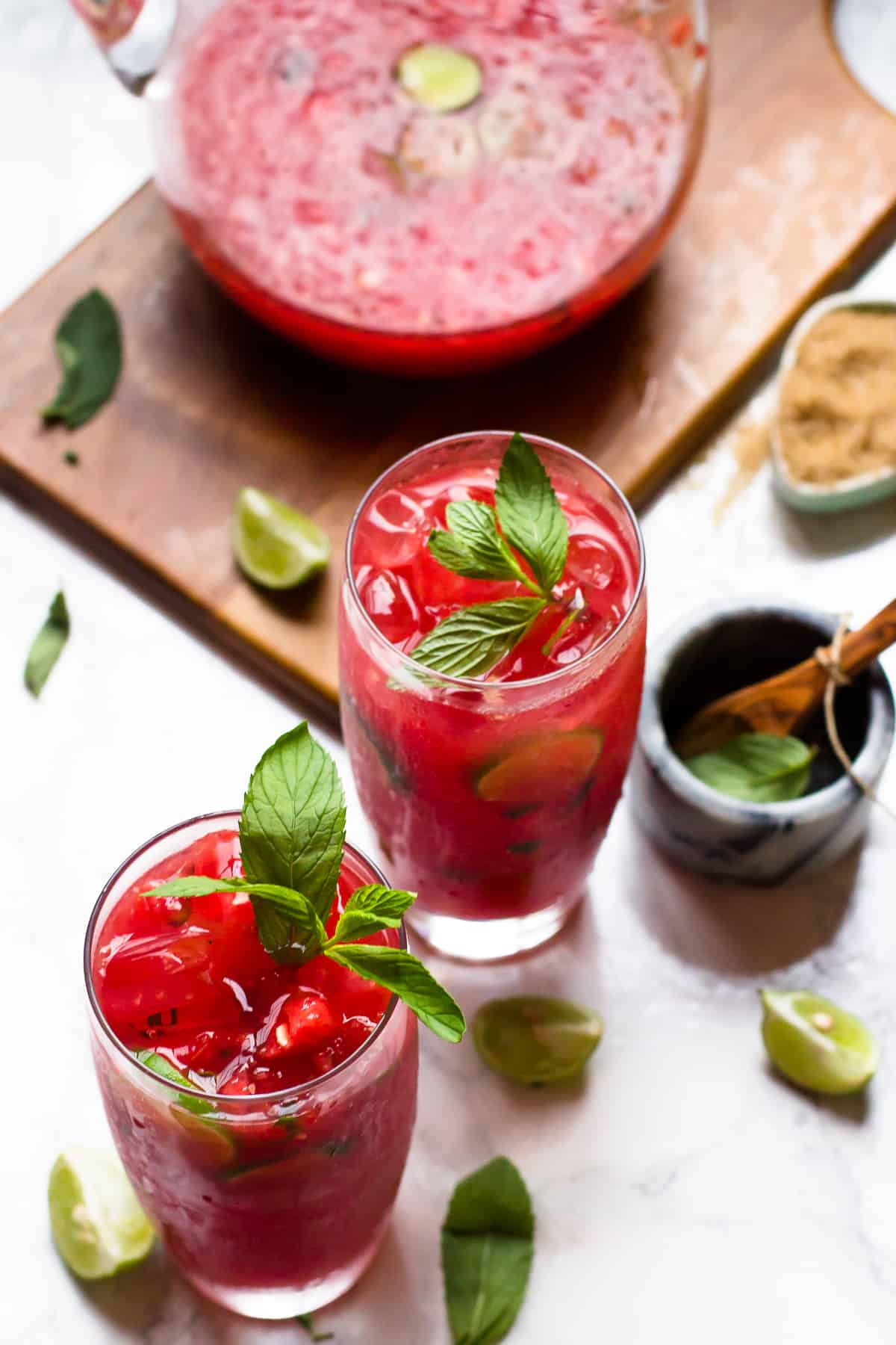 Two glasses of watermelon mojitos with sprigs of mint in them.