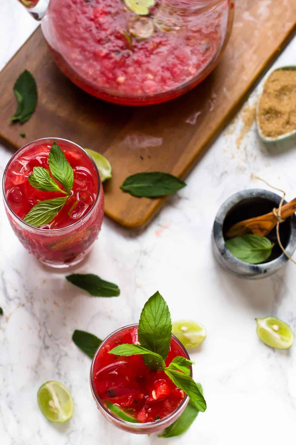 Two watermelon mojitos with pitcher on wood board