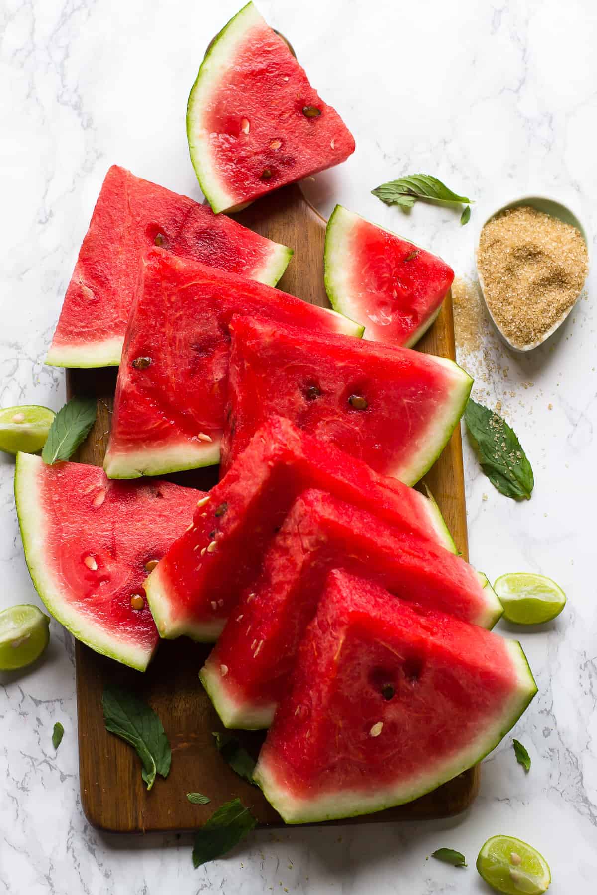 Wedges of watermelon on cutting board with lime wedges and mint leaves
