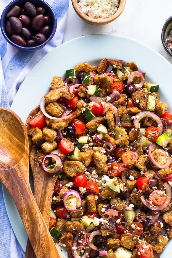 Top downs shot of greek panzanella salad on a long dish with wooden spoon on the side. 