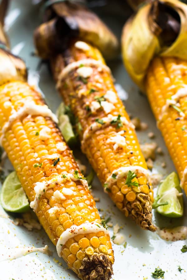 Close up of grilled mexican street corn on a white plate with wedge of lime. 