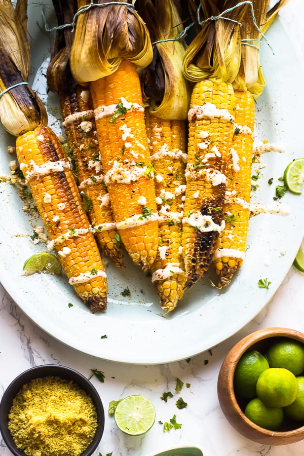  Overhead shot of grilled mexican street corn on a white dish with a bowl of limes. 