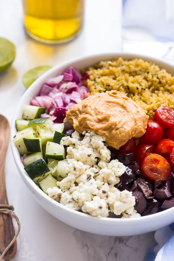 Mediterranean quinoa salad bowl on a table with a wood spoon and lime wedges on the side. 