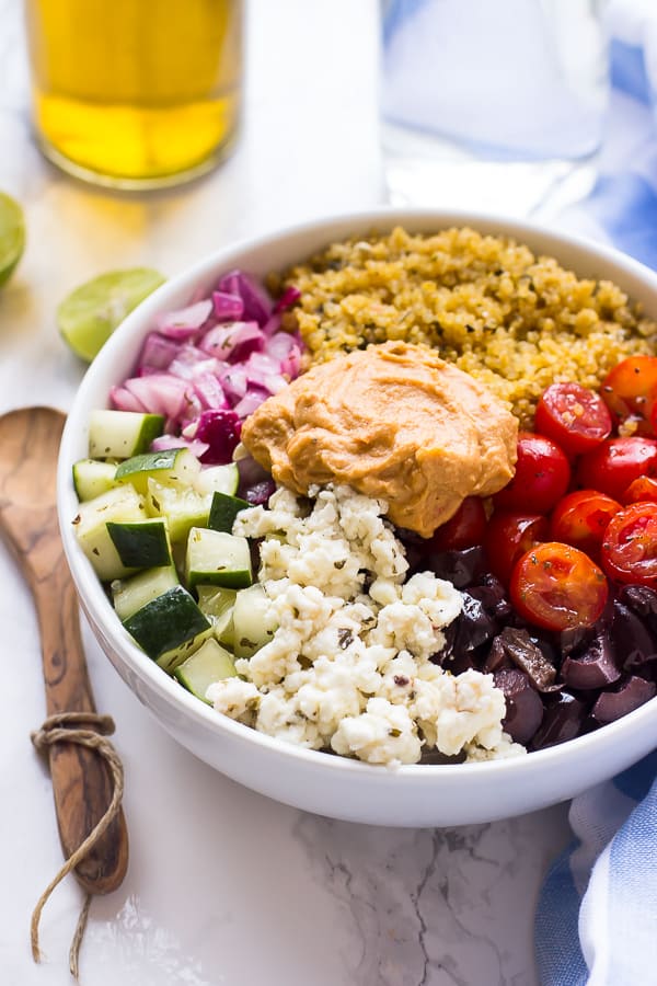 A mediterranean quinoa bowl on a table with lime wedges. 