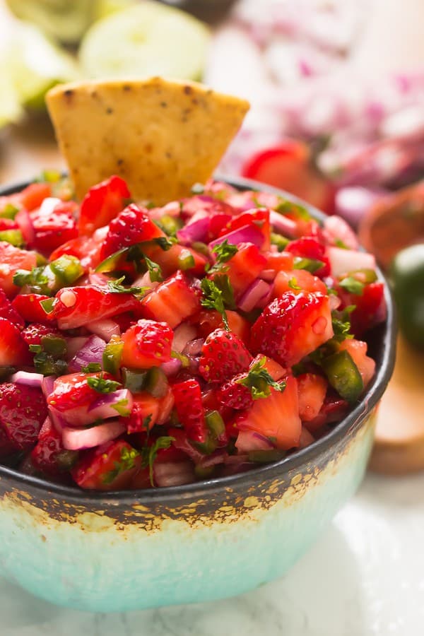 Close up of strawberry jalapeno salsa in a bowl with a tortilla chip dipped in. 