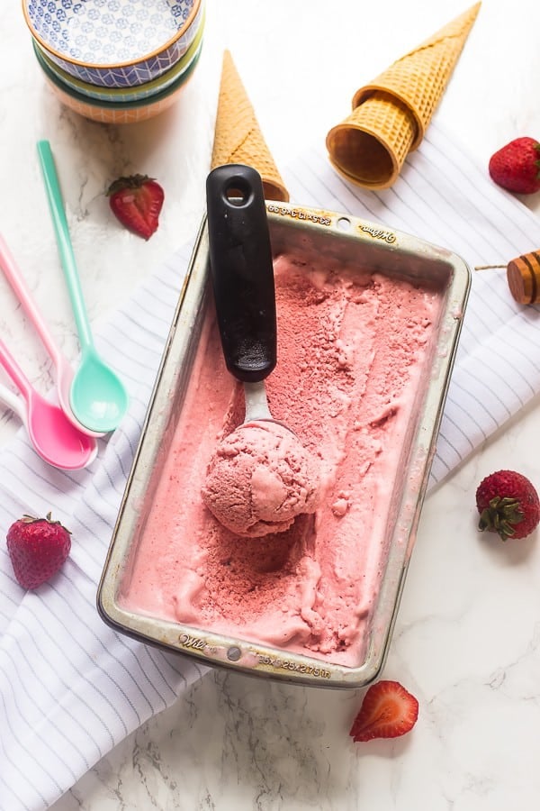 Overhead view of strawberry ice cream in a tub with an ice cream scoop. 