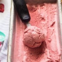 Vegan strawberry ice cream being scooped from a tub.